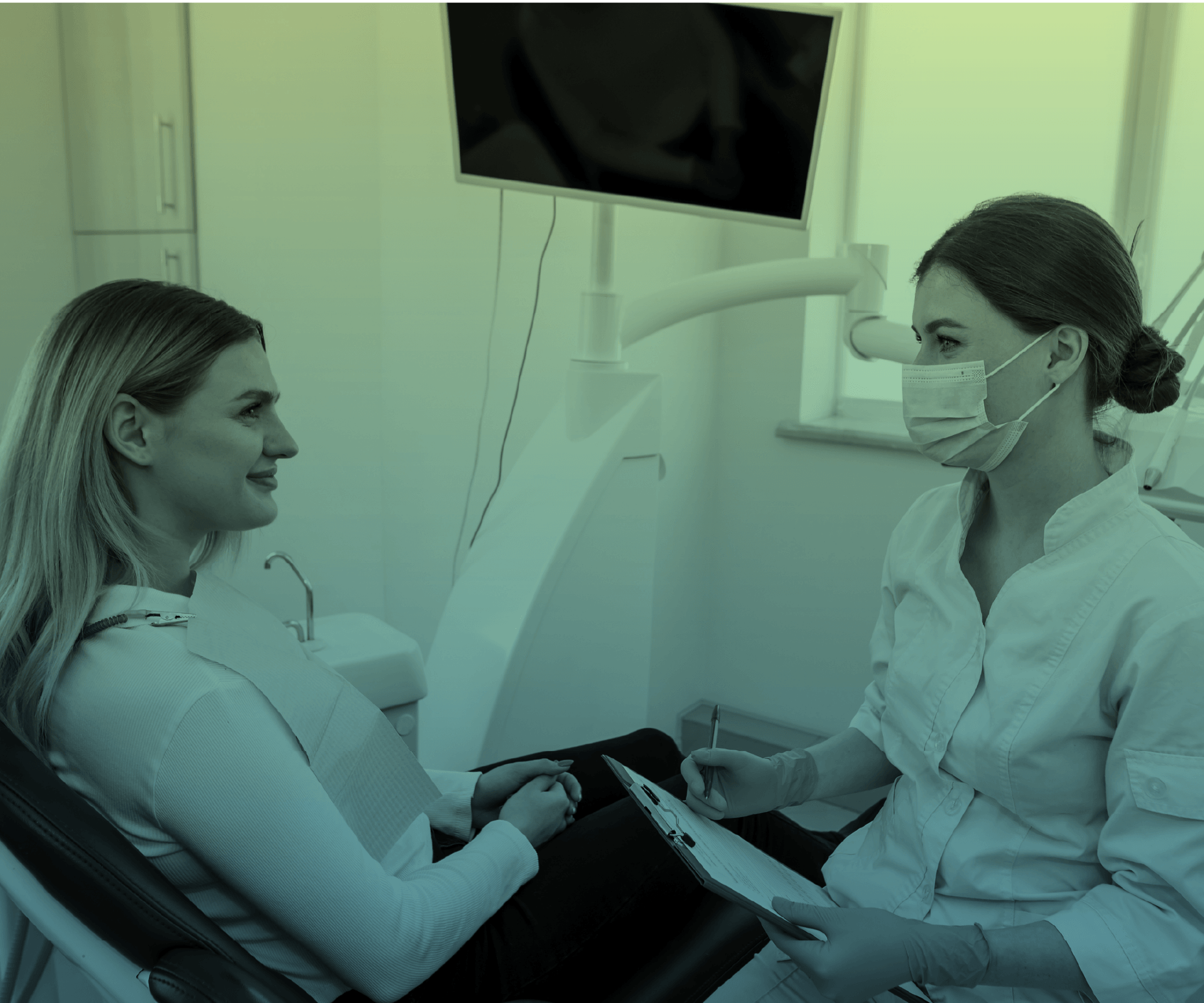 A dental assistant in scrubs talking with a patient in a clinical setting.